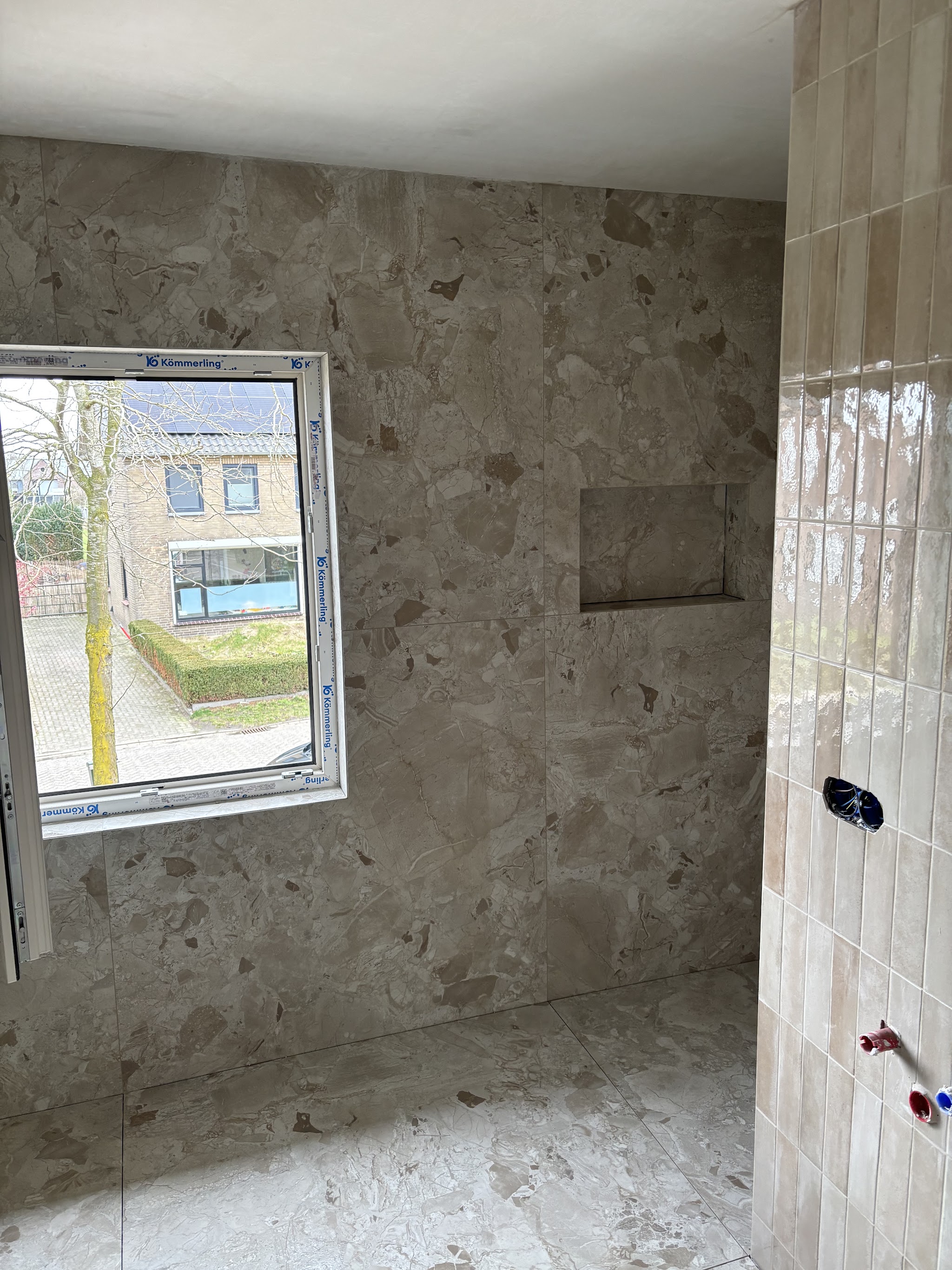 Wand met terrazzolook tegels en een ingebouwde nis, naast staande beige wandtegels